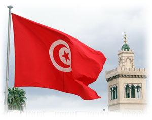 Die Flagge Tunesiens zeigt einen Mond und einen Stern in einem Kreis. Die rot-weiße Flagge Tunesiens vor blauem Himmel im Wind.